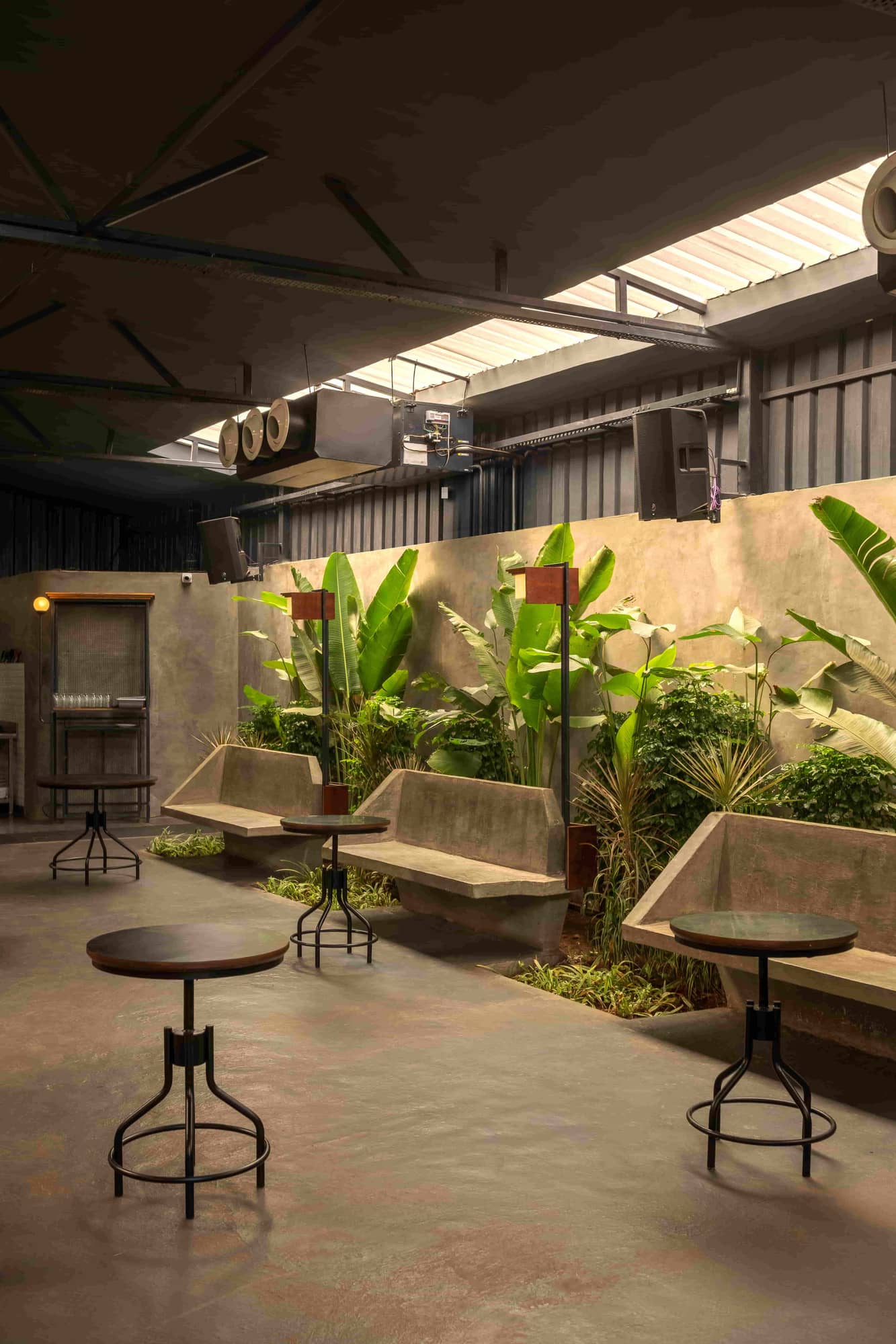 The main room: concrete benches, a long planter under the skylight, tables and steel chairs